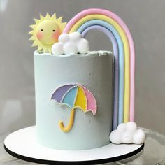 there is a cake with an umbrella and clouds on the top, next to a rainbow