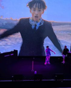 a man standing on top of a stage in front of a large screen with his hands out