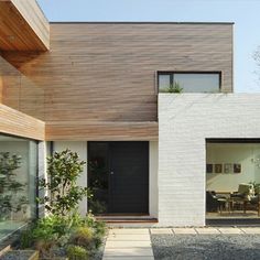 a black door is in front of a white brick building with trees and plants on the side