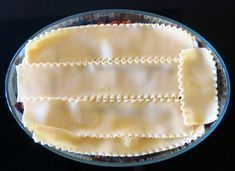 an uncooked ravioli in a glass dish on top of a black surface