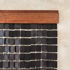 a wall hanging made out of black leather squares and wooden pegs on a white wall