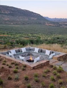 an outdoor fire pit surrounded by rocks in the middle of a field with mountains in the background