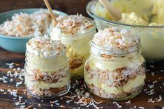 four jars filled with desserts on top of a wooden table