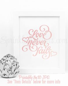 a white frame with the words love never falls on it next to a silver vase