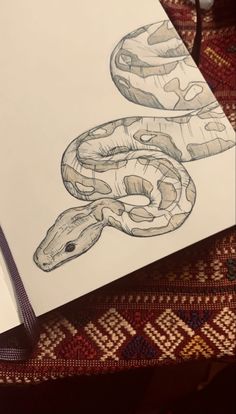 a drawing of a snake on top of a white paper next to an open book