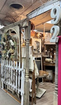 a store front with lots of items on display in the window and behind it is a white picket fence