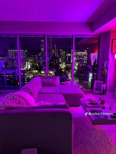 a living room with purple lighting and large windows overlooking the city lights at night time