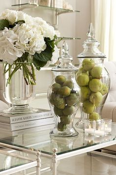 a glass table topped with two vases filled with flowers and fruit next to books