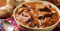 a bowl filled with stew next to bread