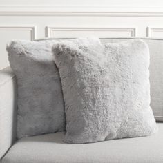 two pillows sitting on top of a couch next to a white headboard and wall