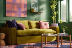 a living room with green walls and colorful pillows on the couch, coffee table and potted plant