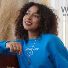 a woman with curly hair wearing a blue sweatshirt sitting on a bench and smiling at the camera