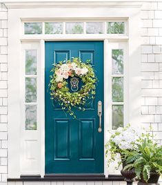 a blue front door with a wreath on it and two potted plants next to it