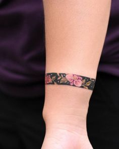 a woman's wrist with a flowered bracelet on her left hand and a purple shirt on the right