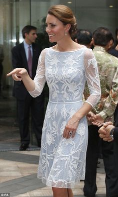 a woman in a white dress pointing at something while standing on the sidewalk with other people behind her