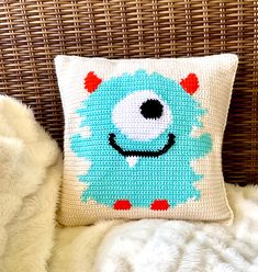 a blue monster pillow sitting on top of a white fur covered bed next to a wicker chair