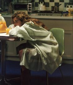 a woman sitting at a table in front of a glass jar with liquid on it