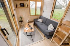 a couch and table in a small living room with wood floors, windows, and stairs