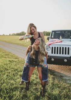 two women are standing in front of a jeep and one is holding another woman's head