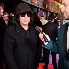 a man in a suit and hat holding a microphone next to a woman wearing sunglasses