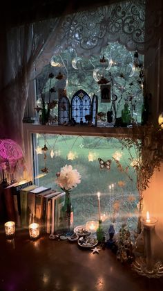 a shelf with candles, flowers and books in front of a window filled with fairy lights