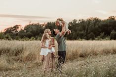 a family standing in a field at sunset with one holding the child up to his head