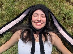 a woman laying in the grass wearing a hat and scarf