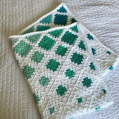 a crocheted blanket is laying on top of a bed with white sheets and green shamrocks