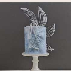 a frosted blue cake sitting on top of a white pedestal next to a gray wall