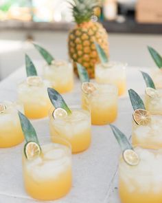 pineapple and lemonade cocktails are arranged on a white table with green leaves