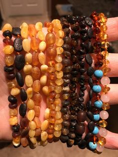 a person's hand holding several bracelets with different colored beads and stones on them