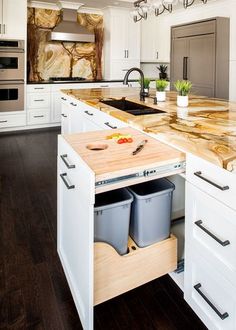 a kitchen with white cabinets and wooden counter tops, two trash cans on the island