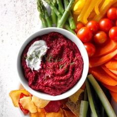 a white bowl filled with red dip surrounded by veggies