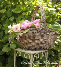 a wicker basket with pink flowers sitting on top of a small table in front of some bushes