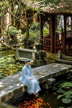 a woman sitting on a stone bench next to a pond filled with goldfish