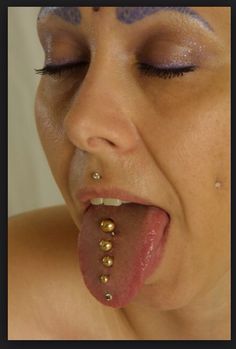 a woman sticking her tongue out with piercings on her face and nose, while wearing gold jewelry