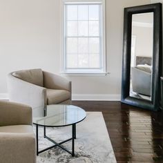 a living room with two chairs and a table in front of a mirror on the wall