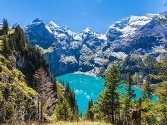 a mountain lake surrounded by trees and snow covered mountains with blue water in the distance