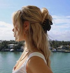 a woman standing on top of a boat next to the ocean with her hair in a pony tail