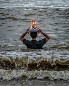 a man in the water holding a small child on his head with an elephant on top