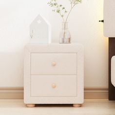 a white night stand with two drawers and a small vase filled with baby's breath flowers