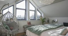 a bedroom with a bed, hanging chair and large windows