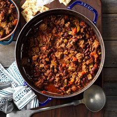 two bowls filled with chili and cheese next to crackers on a wooden table top