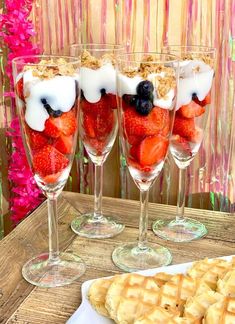 three glasses filled with strawberries, blueberries and yogurt on top of a wooden table