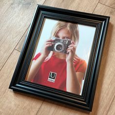 a framed photograph of a girl holding a camera in front of her face on the floor