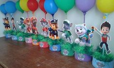 there are many balloons on the wall and some paw patrol figures in pots with grass