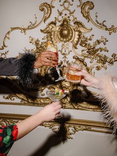 two people are toasting with drinks in front of a fancy wall