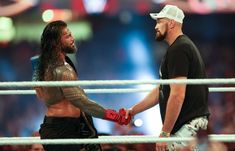 two men shaking hands while standing next to each other in front of an audience at a wrestling match