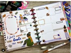 an open planner book sitting on top of a wooden table next to markers and pens