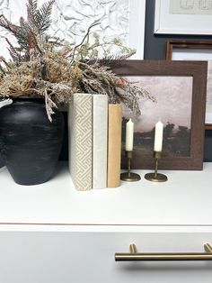 some books and candles are sitting on a white shelf next to a potted plant